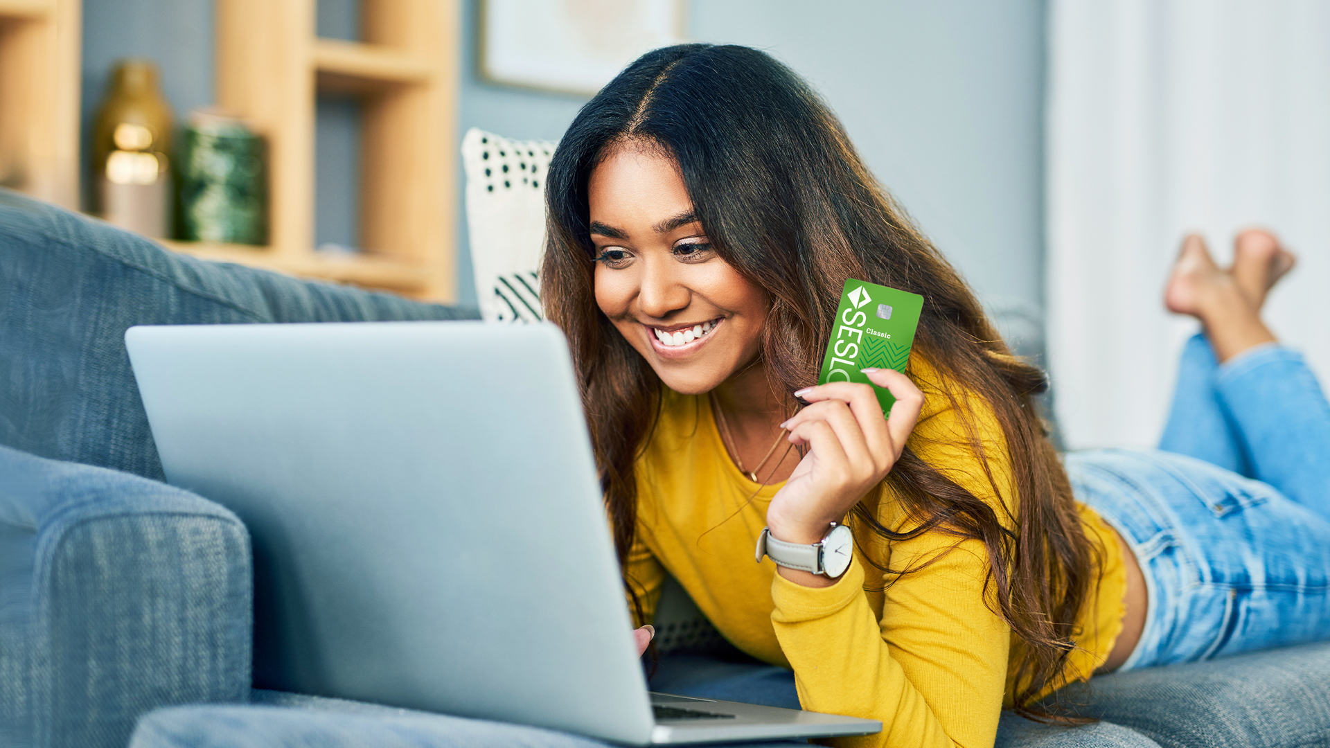 Woman on couch shopping online with her SESLOC Visa credit card