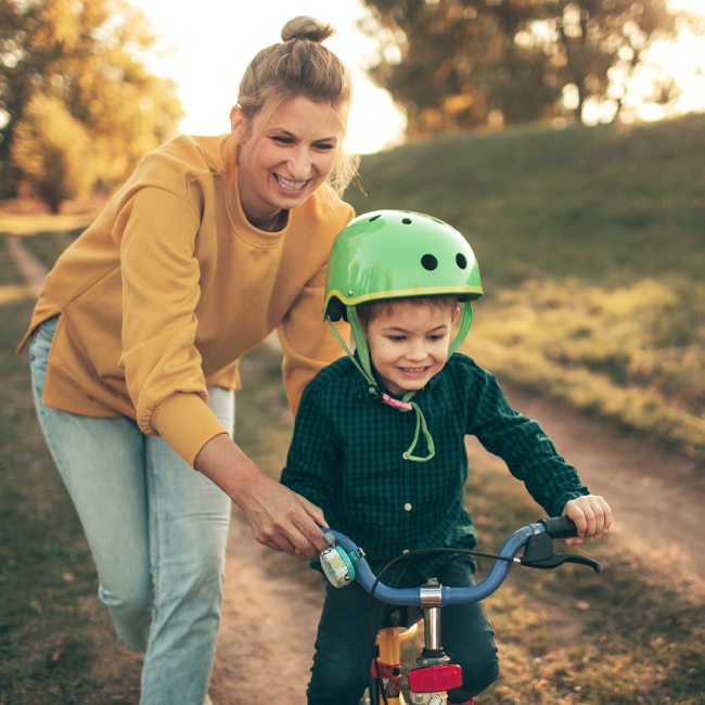 Mother help little boy learn to ride a bike.