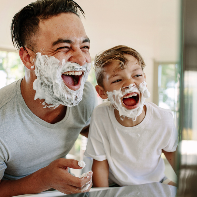 Father and son having fun pretending to shave in the mirror.
