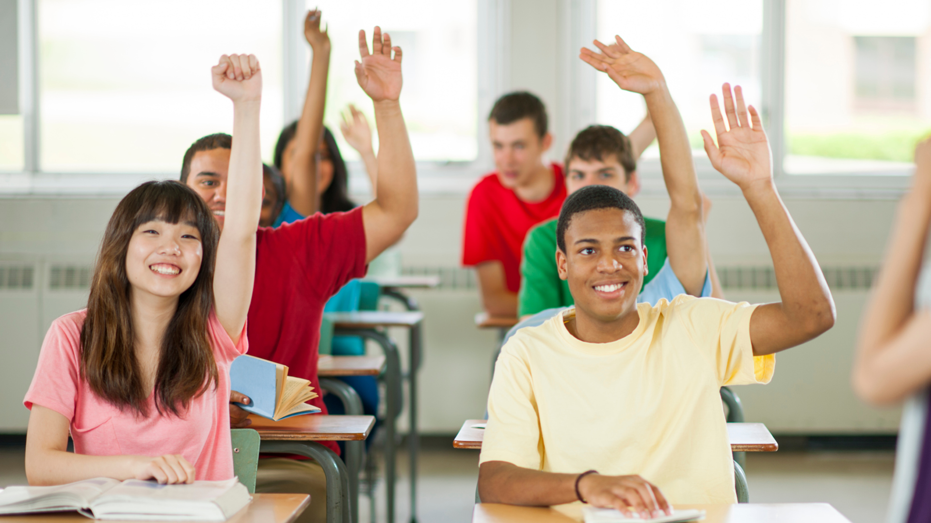 Students in a classroom raise their hands.