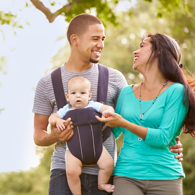 A young couple with a baby stroll through a park.